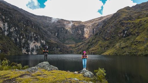 Two people standing next to a tranquil lake in the evergreen mountains