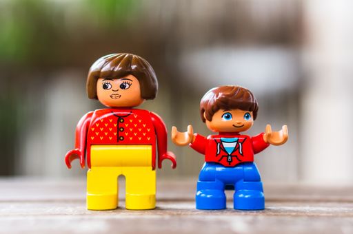 Lego Duplo woman and child figurines standing on a wooden surface in soft focus background