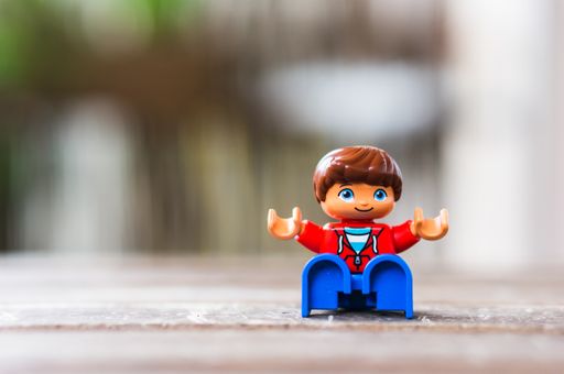 Lego Duplo boy figurine sitting on a wooden surface in soft focus background
