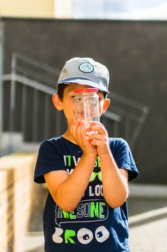 Six years old Polish Caucasian boy looking into a glass jar with bugs on a sunny day
