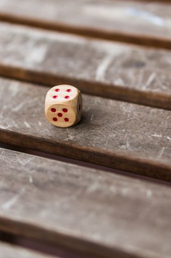 A vertical closeup shot of a wooden die with red dots on a brown surface