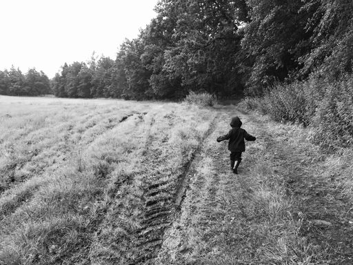 A grayscale shot of a lost little boy running around in a vast field in the countryside alone