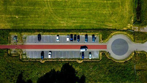 An aerial top shot of a parking lot surrounded by green meadow