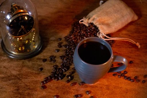 A top view of spilled roasted coffee beans from the bag next to a cup of coffee