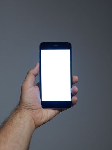 A vertical shot of man's hand holding a phone with white screen with copy space on gray background