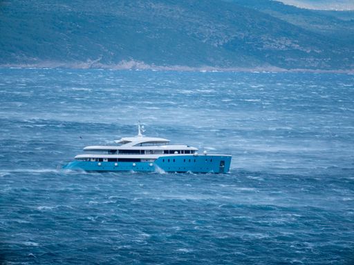 A side view of white and blue cruiser in the blue sea with mountain in the background