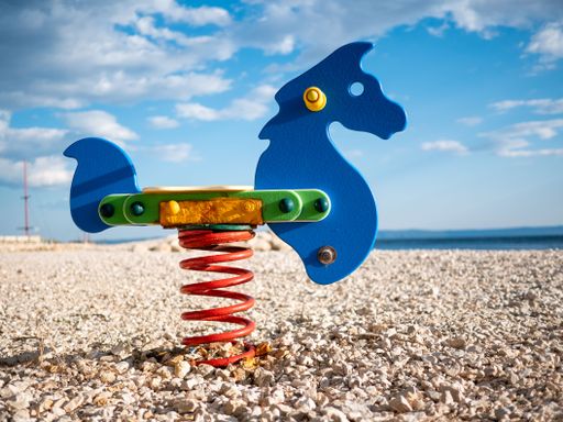 A colorful horse spring rider on the rocky beach under blue cloudy sky