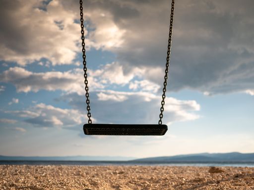A selective focus shot of black swing on metal spring on rocky beach under blue cloudy sky