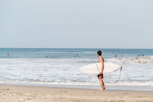 A surfer man holding surfboard and walking on the beach in Puerto Escondido, Mexico