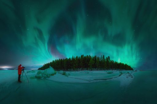 A view of a man photographing a beautiful aurora over a snowy field