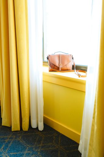 A vertical shot of a brown leather purse on a sunny windowsill in a yellow room