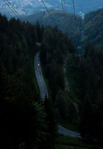 A vertical aerial shot of a path in mountains covered with trees