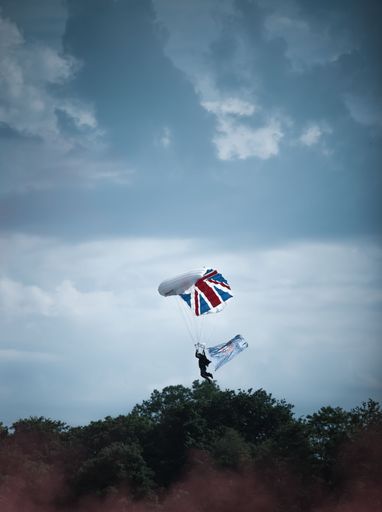 A vertical shot of a parachute with a flag of Great Britain flying over the trees