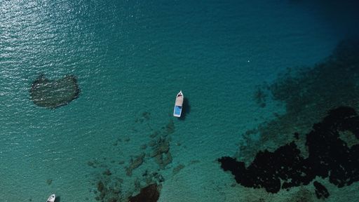 An aerial top view of a boat sailing in a turquoise sea on a sunny day