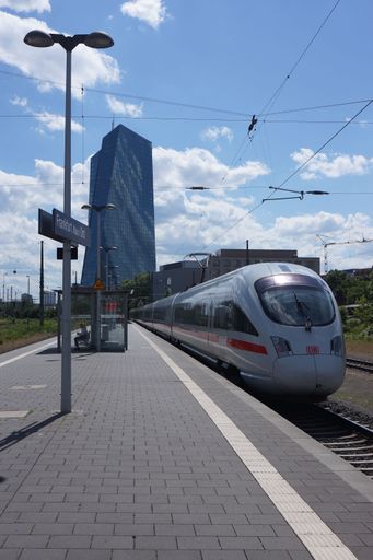 An ICE-T passes through Frankfurt-Ost station, with the European Central Bank in the background.  A sunny summer day with clouds.