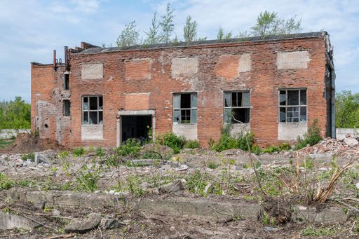 Old industrial workshop made of red brick, dilapidated, in disrepair with broken windows and doors against background of blue summer sky