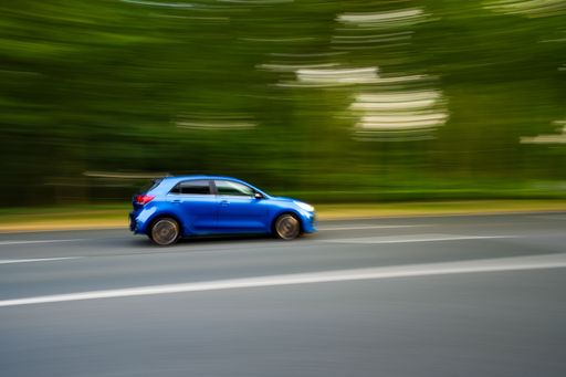 A blue car driving on the road with trees in a motion blur