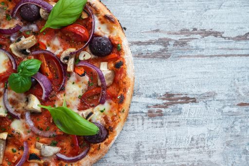 A top view of a delicious pizza with mushrooms, onions, tomatoes, and cheese on a wooden table