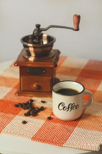 A vertical closeup shot of a coffee mug, a vintage coffee grinder, and coffee beans on the table