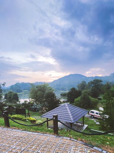 A scenic vertical shot of a gazebo with a lake surrounded by woodlands in the background in the Forest Research Institute of Malaysia, Kepong