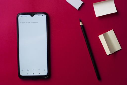 A high angle shot of a phone and pencil on a pink background