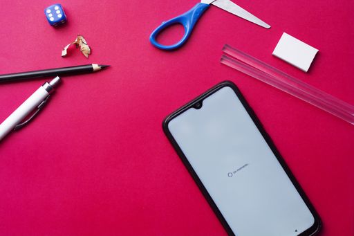 A high angle shot of a phone and school supplies on a pink background