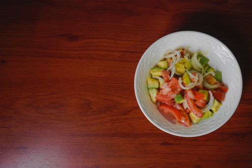 A top view isolated shot of a plate with avocado and tomato salad on wooden table
