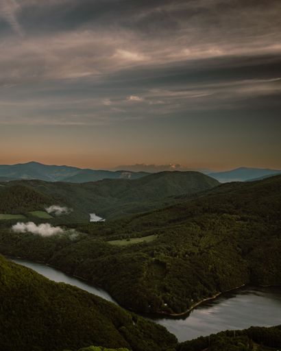 A vertical shot of huge greenery mountains surrounded by water during susnet