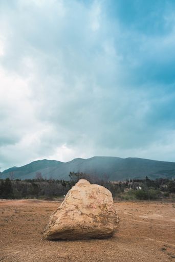 A vertical shot of a stone on an arid environment with mountains on the background on a cloudy day