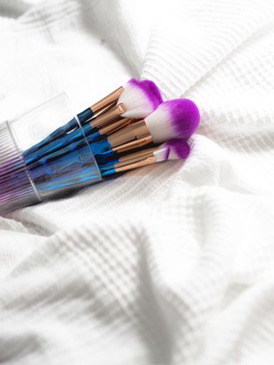A closeup shot of a colorful set of makeup brushes in a glass cup lying on bedsheet