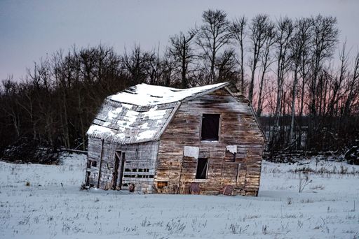 An old wooden barn in a snowy field.