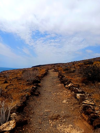 Mountain landscape with narrow path in valley overlooking the sea on island of La Gomera under blue cloudy sky
