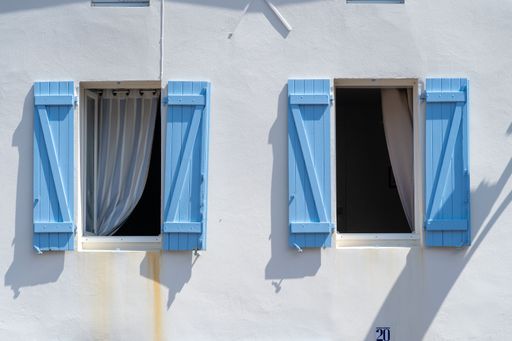 A closeup of a window with blue wooden shutters on the white wall of an old house