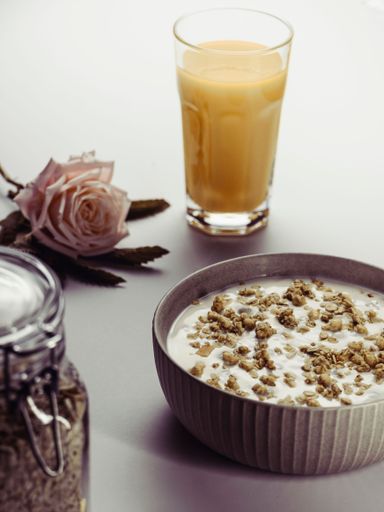 An aesthetic vertical shot of a morning meal with orange juice and a pink rose