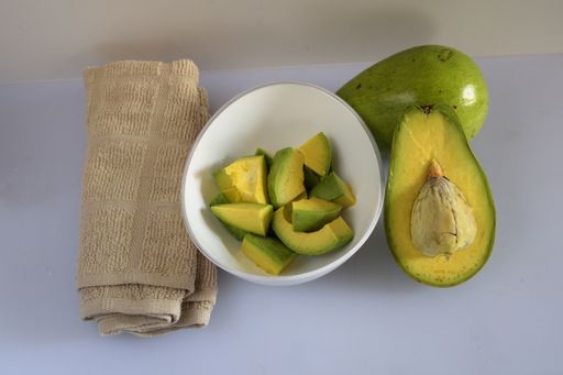 A top view of cut-up pieces of avocado pieces in a bowl and halved avocados on a kitchen table