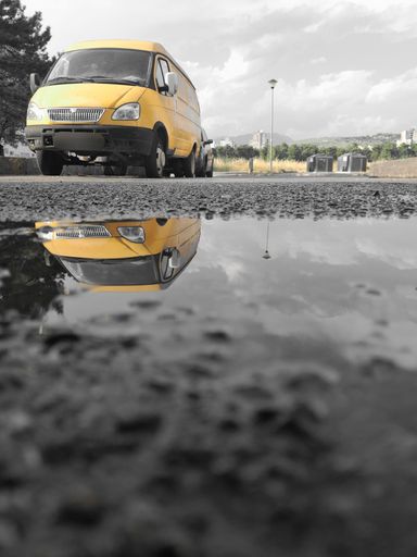 A low-angle shot of a yellow van reflection captured in a water puddle on the street
