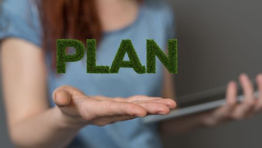 A woman holding the tablet and presenting the 3D rendered green plan word made of grass