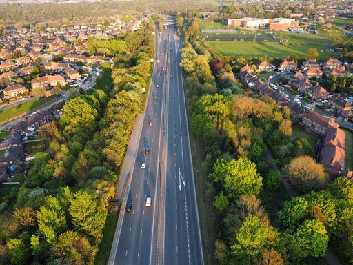 The bird's eye view of the highway with passing cars surrounded by green trees.