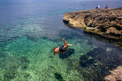 A man jumping from high rock to the sea on a sunny summer day