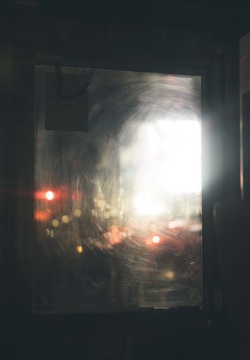 A vertical shot of a scratched up window with blurred lights in the background