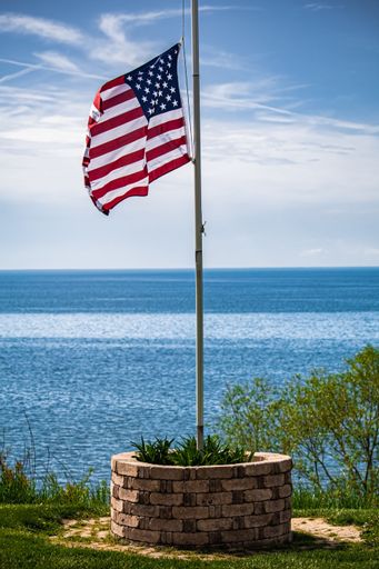 A vertical shot of the American Flag on the flagpole in a well against the background of the Lake Erie