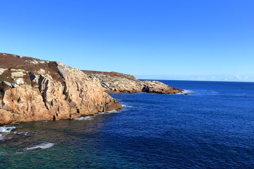 A bird's eye view of rocky cliffs against a blue ocean on a sunny day