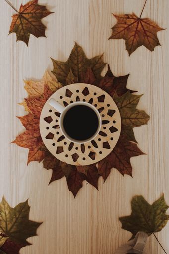 A vertical shot of a cup of coffee with some autumn leaves on a wooden surface