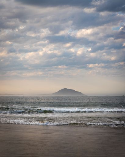 A vertical shot of waves washing the sandy beach with a scenic cloudscape
