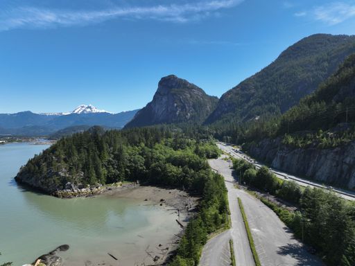 An aerial view of an asphalt highway near a lake against green mountains