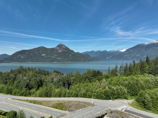 An aerial view of an asphalt highway near a lake against green mountains