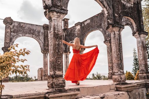 Beautiful young woman in a red dress dancing alone in Water Palace Soekasada Taman Ujung Ruins on Bali Island in Indonesia.