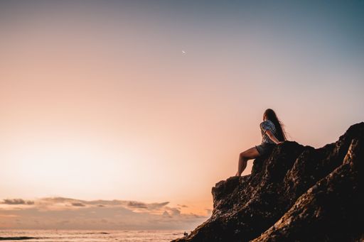 A woman sitting on the edge of the cliff and looking at the beautiful sunset.