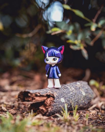A vertical Pop Mart x Yosuke Ueno toy figurine of Iggy the Kit standing on top of a fallen tree log.