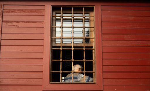 A red wooden house and man resting by its window